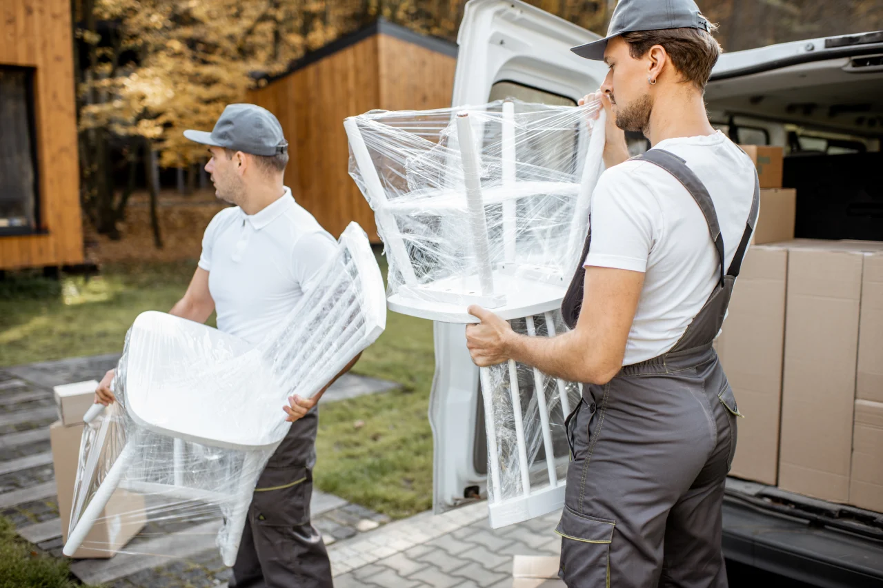 Möbelpacker tragen verpackte Stühle aus dem Transporter